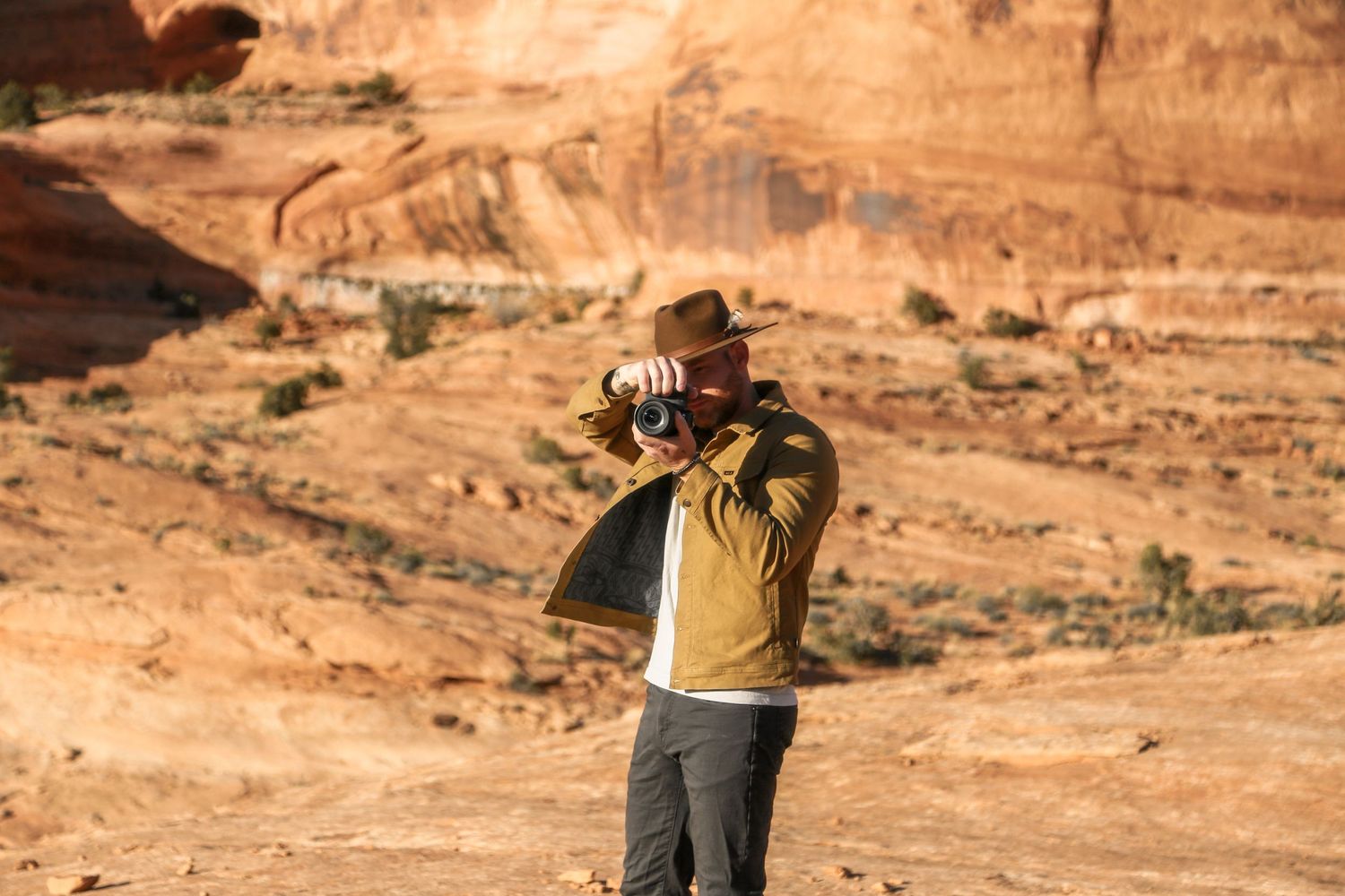 A hiker explores the rugged orange sandstone cliffs and canyons in a desert landscape under blue skies.