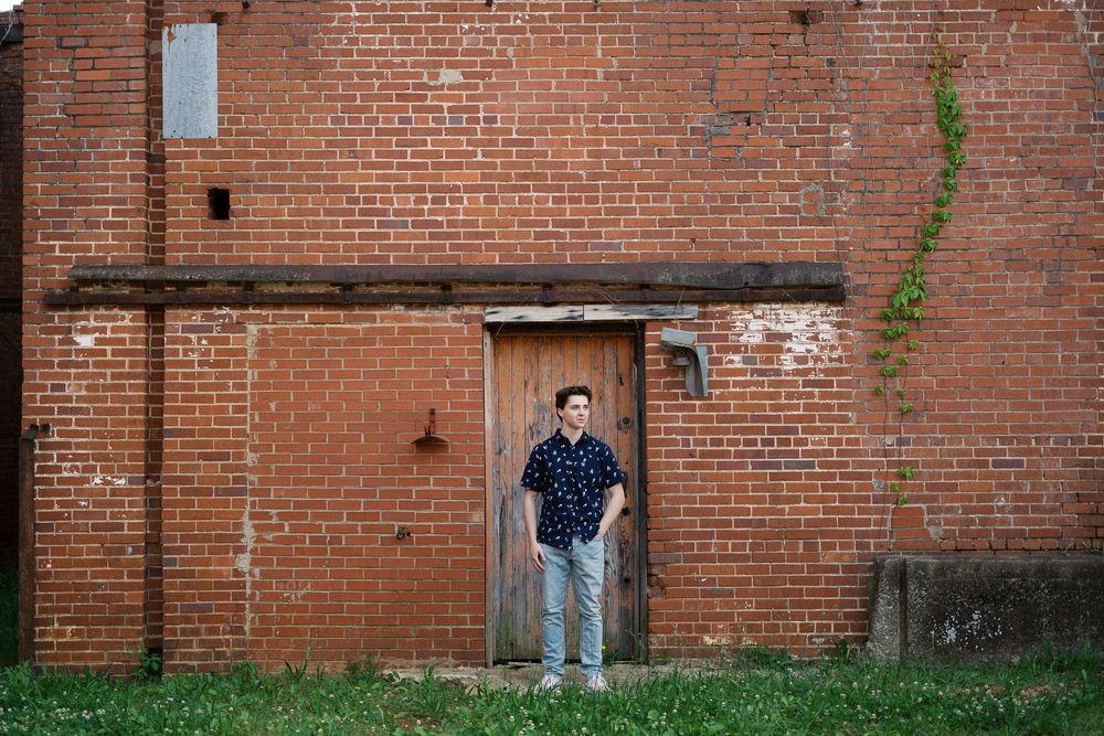 A brick wall with a doorway entrance features someone standing in casual attire against the industrial backdrop.