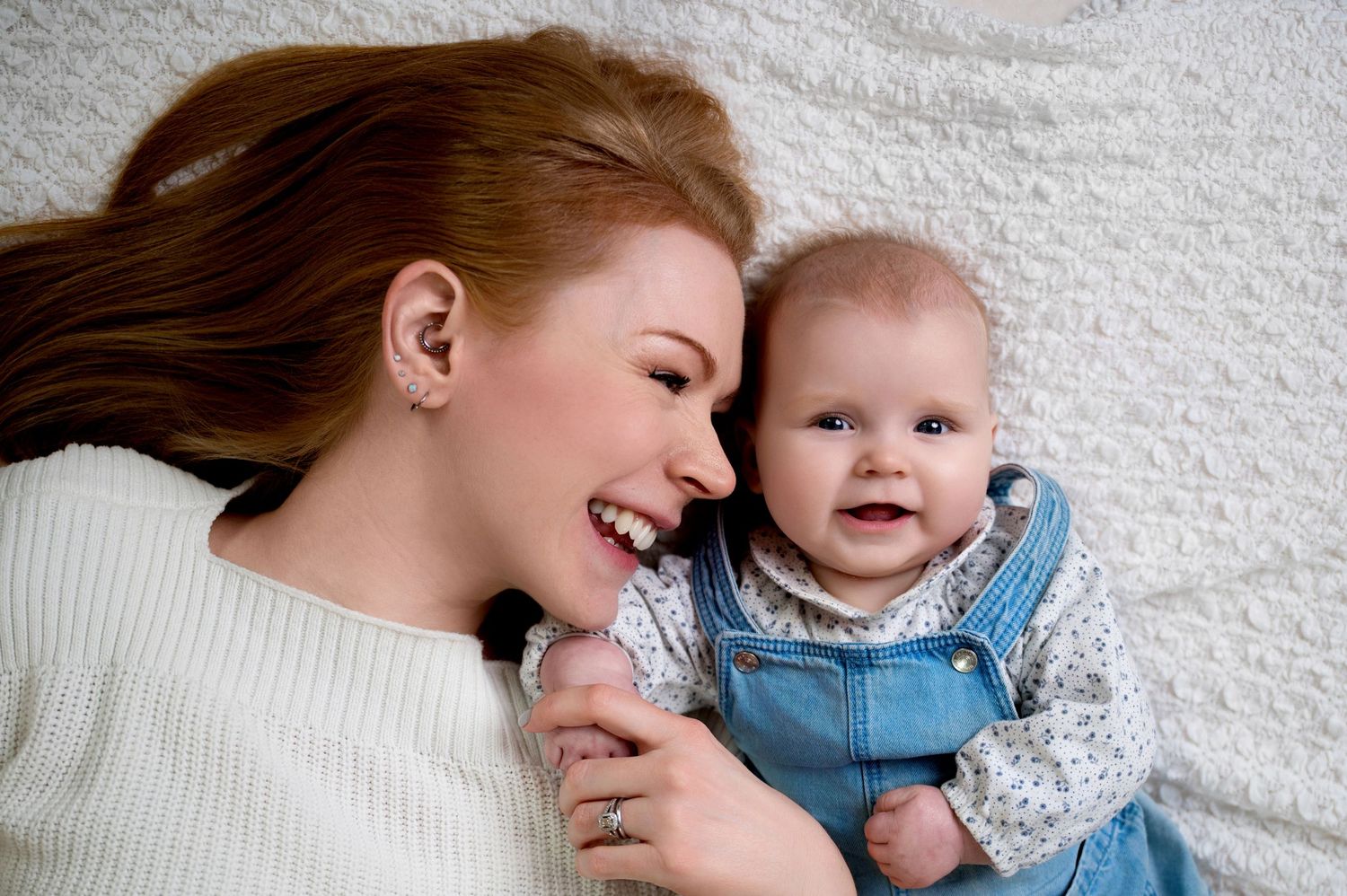A tender bonding moment between parent and baby as they laugh together on a white bed.