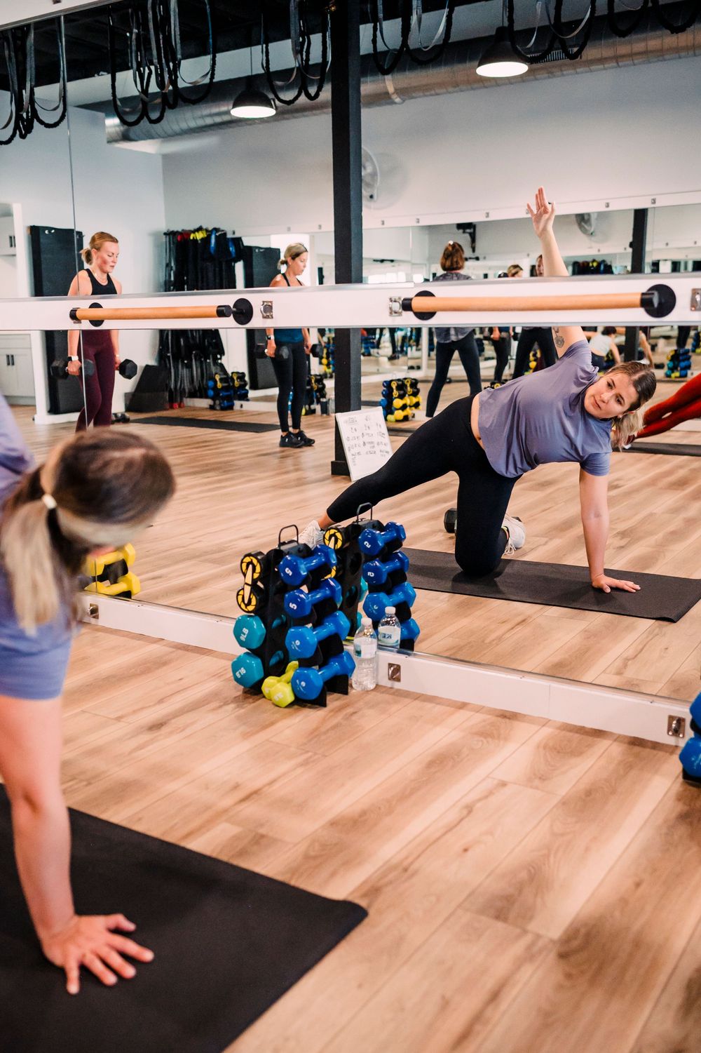 Group fitness class participants performing side plank exercises on yoga mats in a studio.