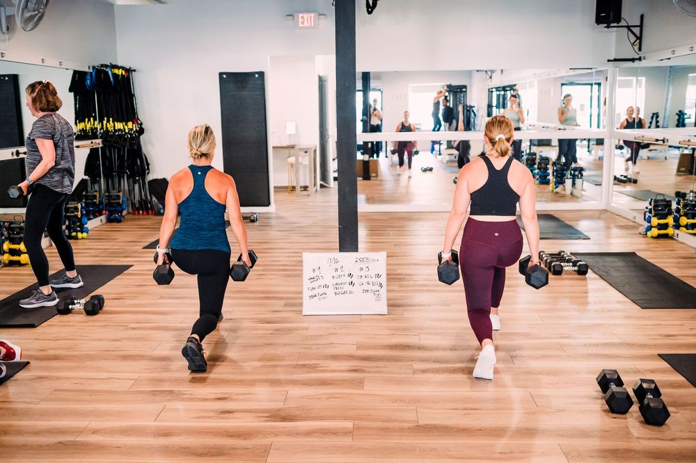 Group fitness class participants walking with dumbbells during a workout session.