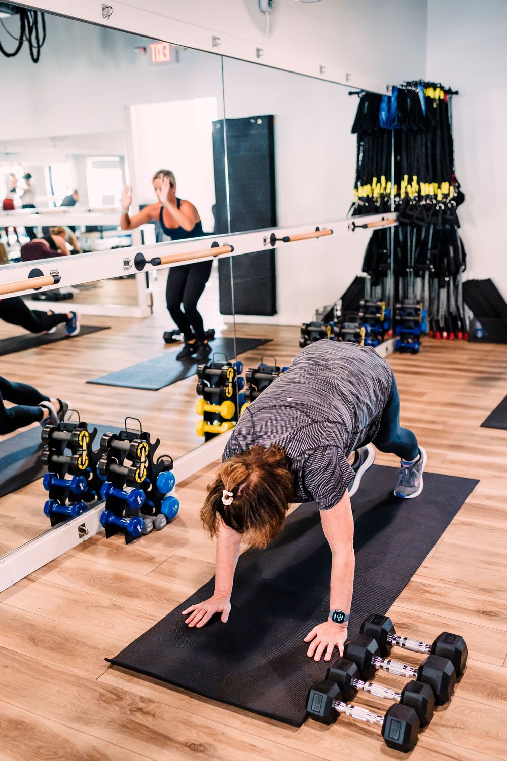 Person doing pushup exercise on black mat with dumbbells in fitness studio.