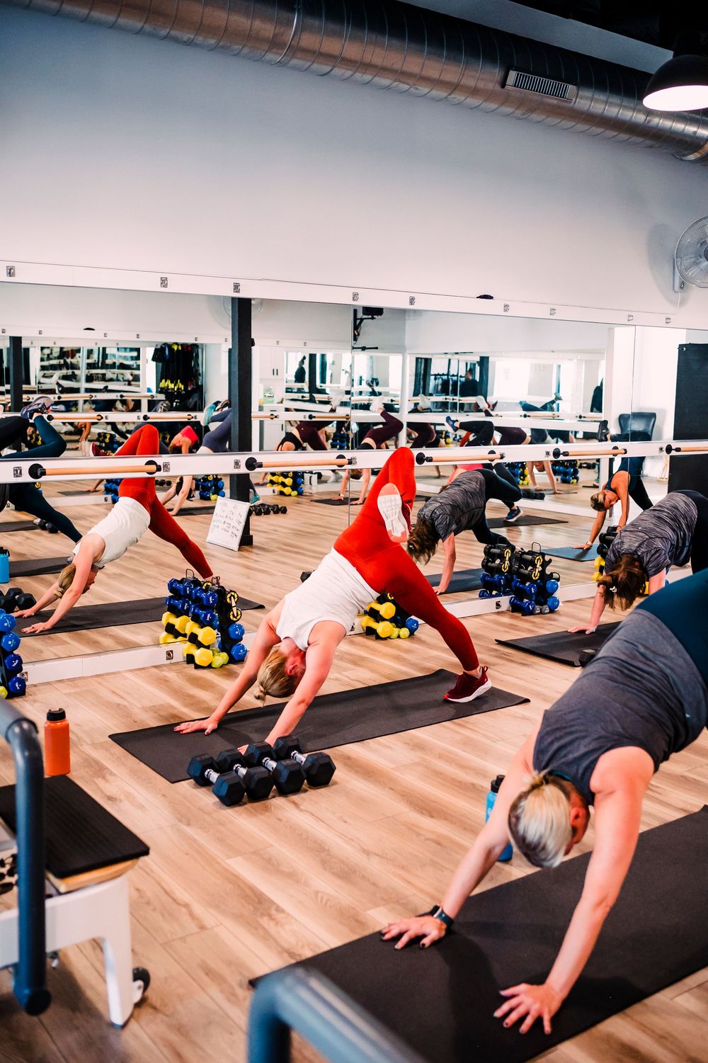 Group fitness class participants in plank position on yoga mats with weights nearby.