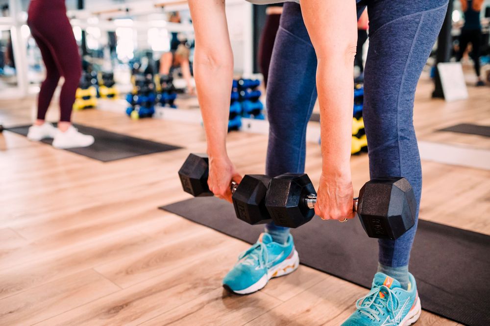 Close-up of legs in athletic shoes during dumbbell exercise on gym floor.