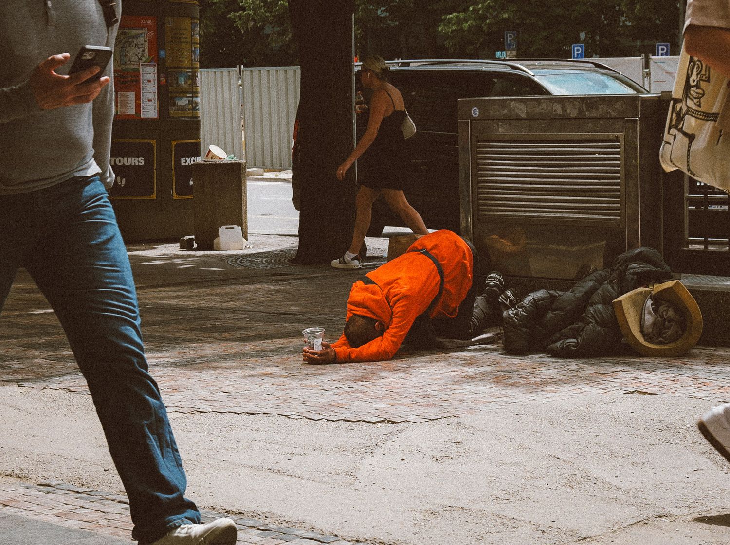 Orange-clad worker rests on the ground next to maintenance equipment on a city street.