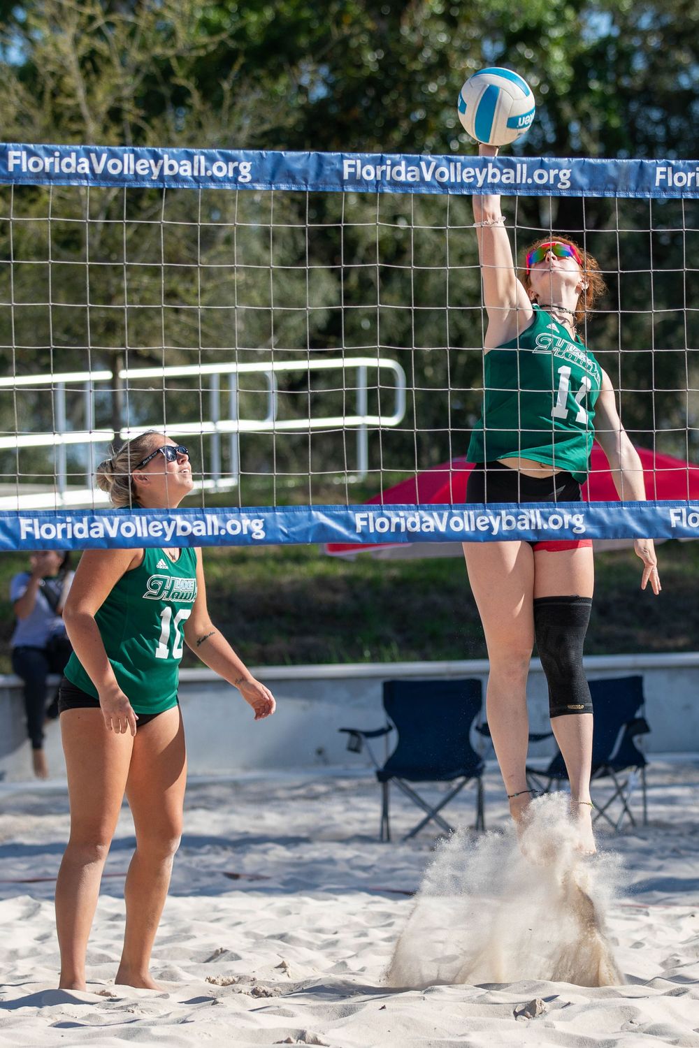 Sand volleyball players competing at beach tournament with FloridaVolleyball.org banners.