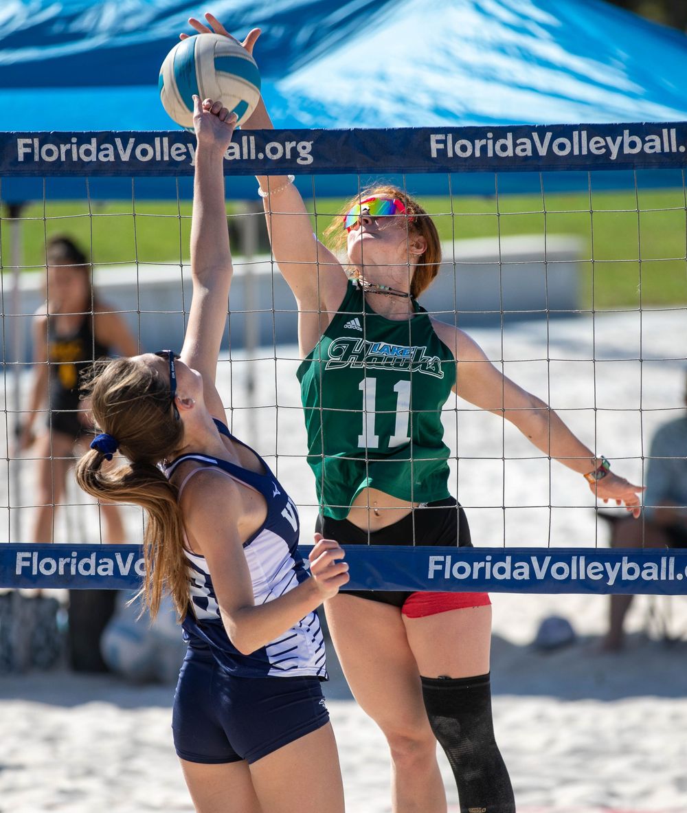 Competitive beach volleyball match with players at the net going for the ball.
