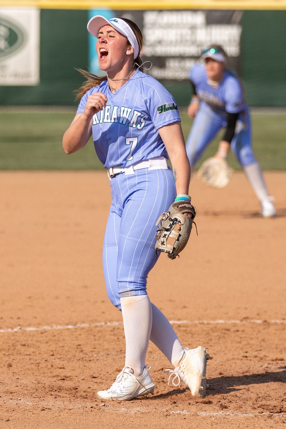 Softball player in light blue uniform celebrating on the field.