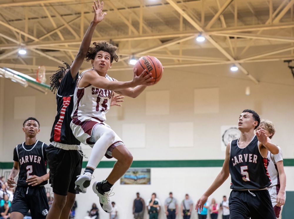 Basketball player leaps for layup during competitive indoor game.