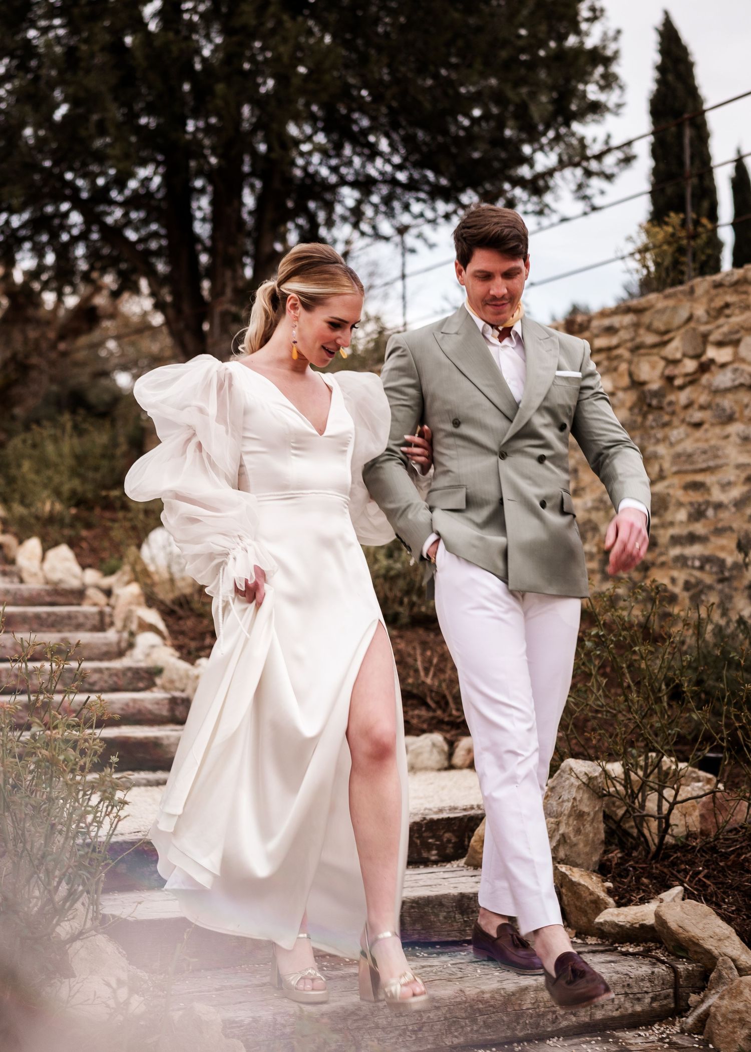 A stylish couple descending stone steps together, the bride in an elegant white dress with puff sleeves.