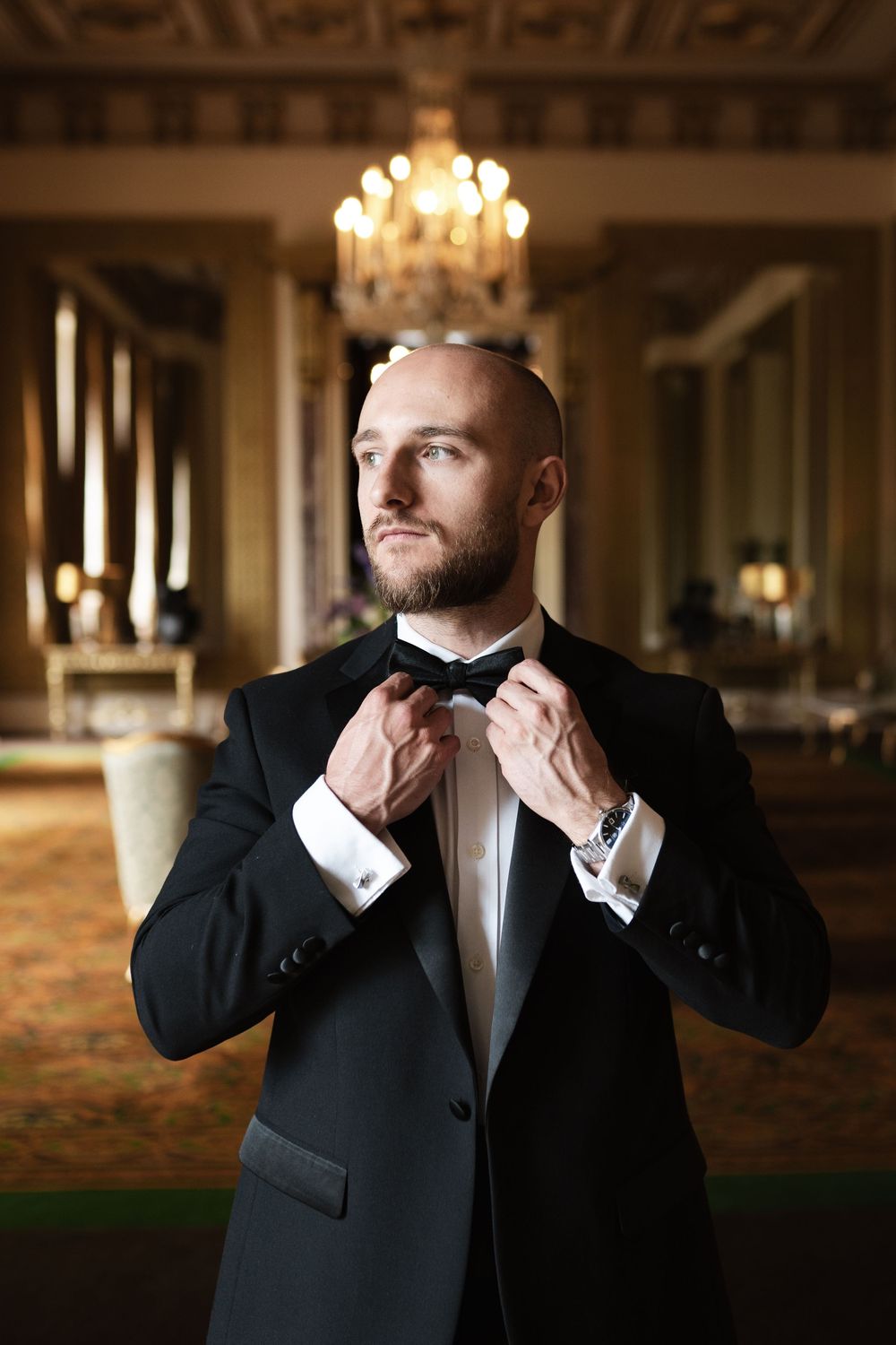 Close-up sequence showing someone adjusting their formal bow tie in an opulent ballroom setting.