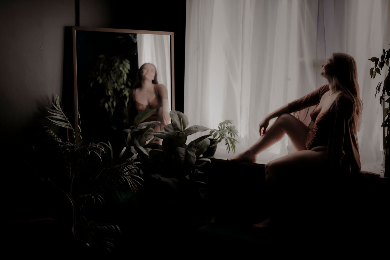 Silhouette reflection in mirror with houseplants creating moody atmospheric composition in dim lighting.