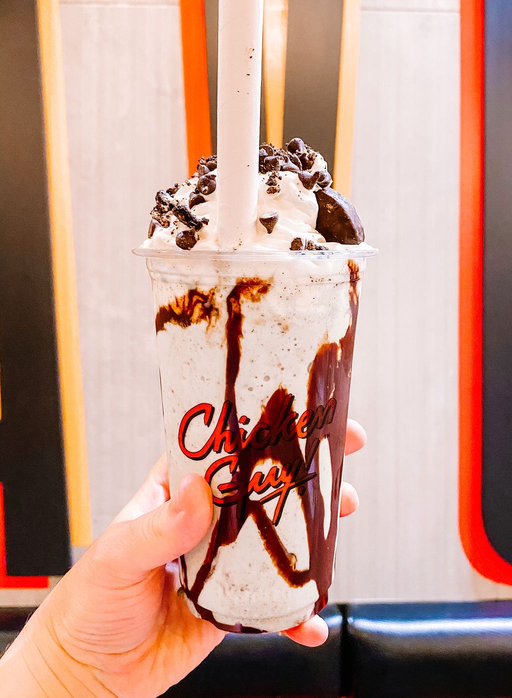 Chocolate-drizzled milkshake topped with whipped cream and cookie crumbs in a clear plastic cup.