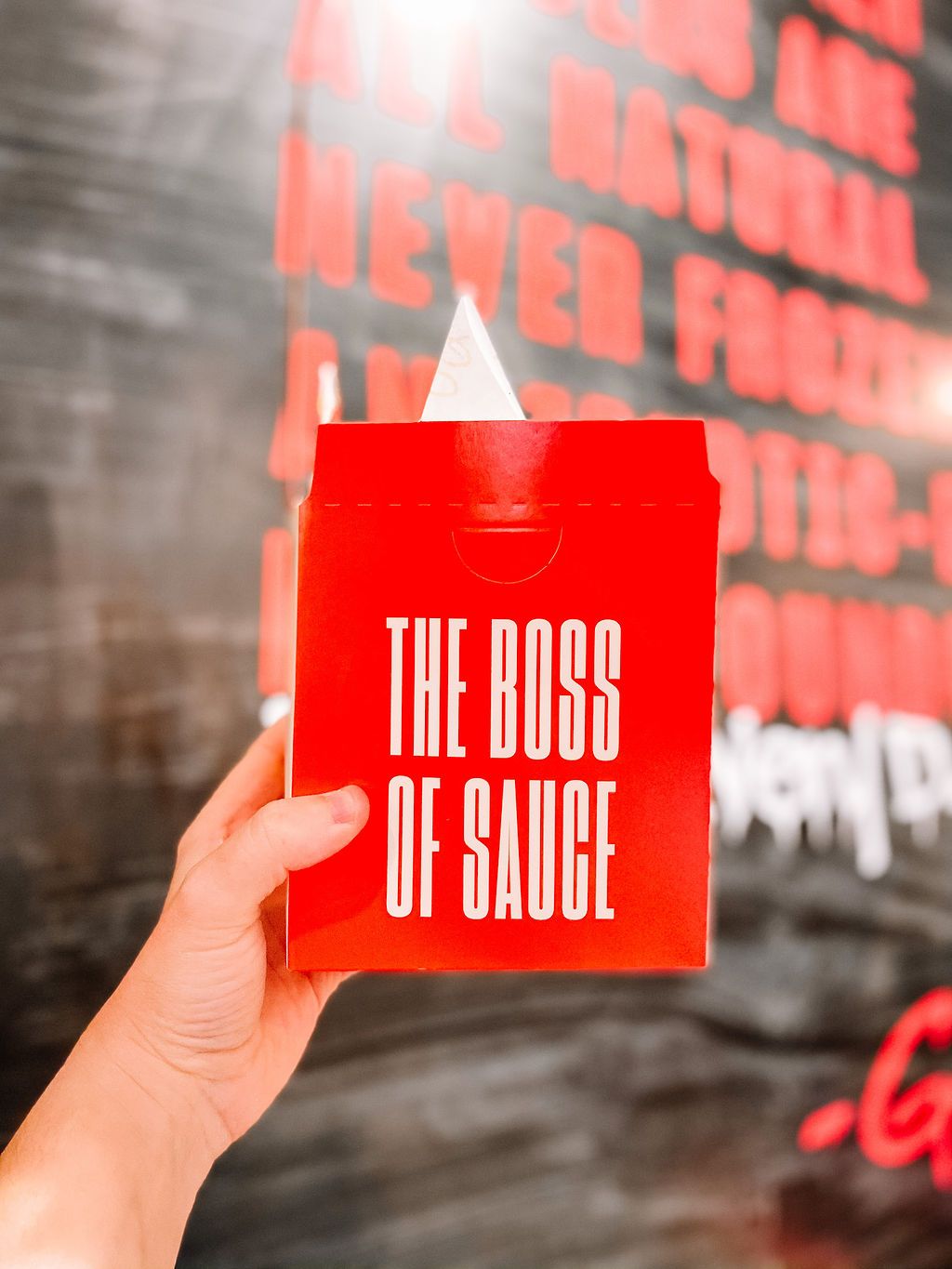 Hand holding red box labeled The Boss of Sauce against textured wall.