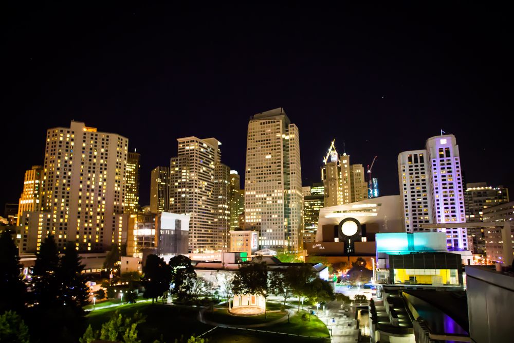 Illuminated modern buildings in a cityscape at night with colorful lights reflecting across the urban skyline.