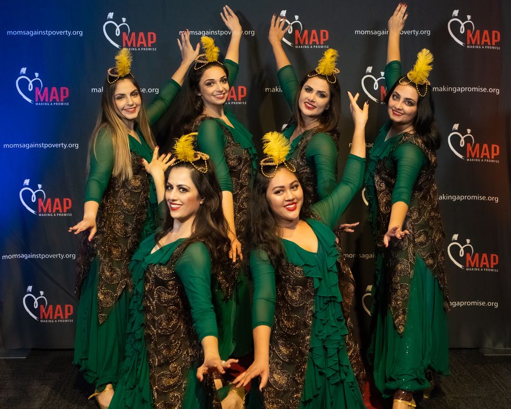 Dance performers in matching emerald green dresses pose with raised arms against branded backdrop at event.