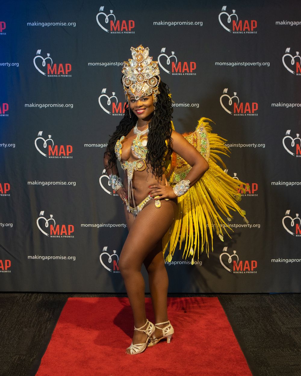 Samba dancer in yellow feathered carnival costume performs on red carpet at MAP event.