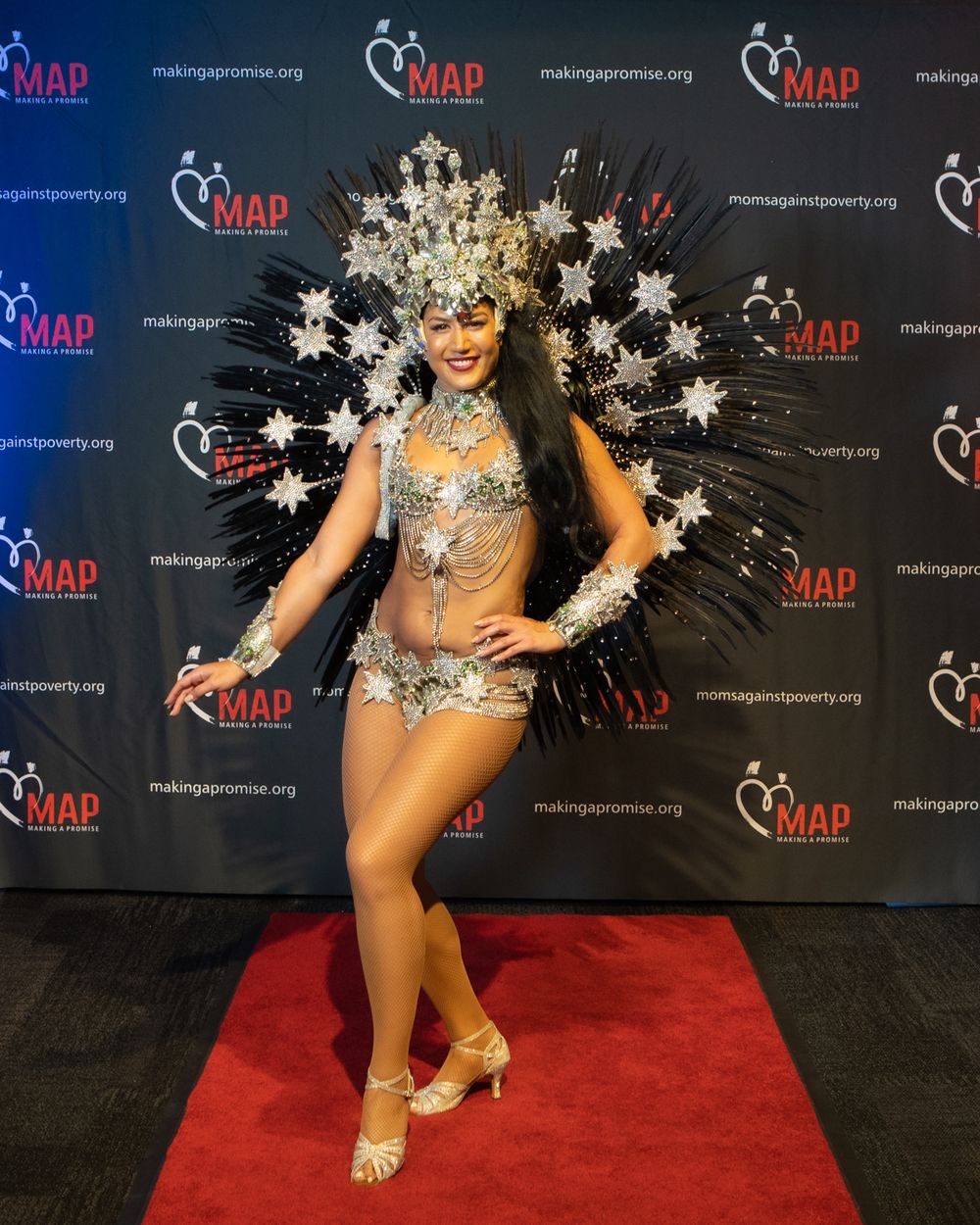 Performer in glittering silver bodysuit and dramatic starburst crown headpiece poses on red carpet at MAP event.