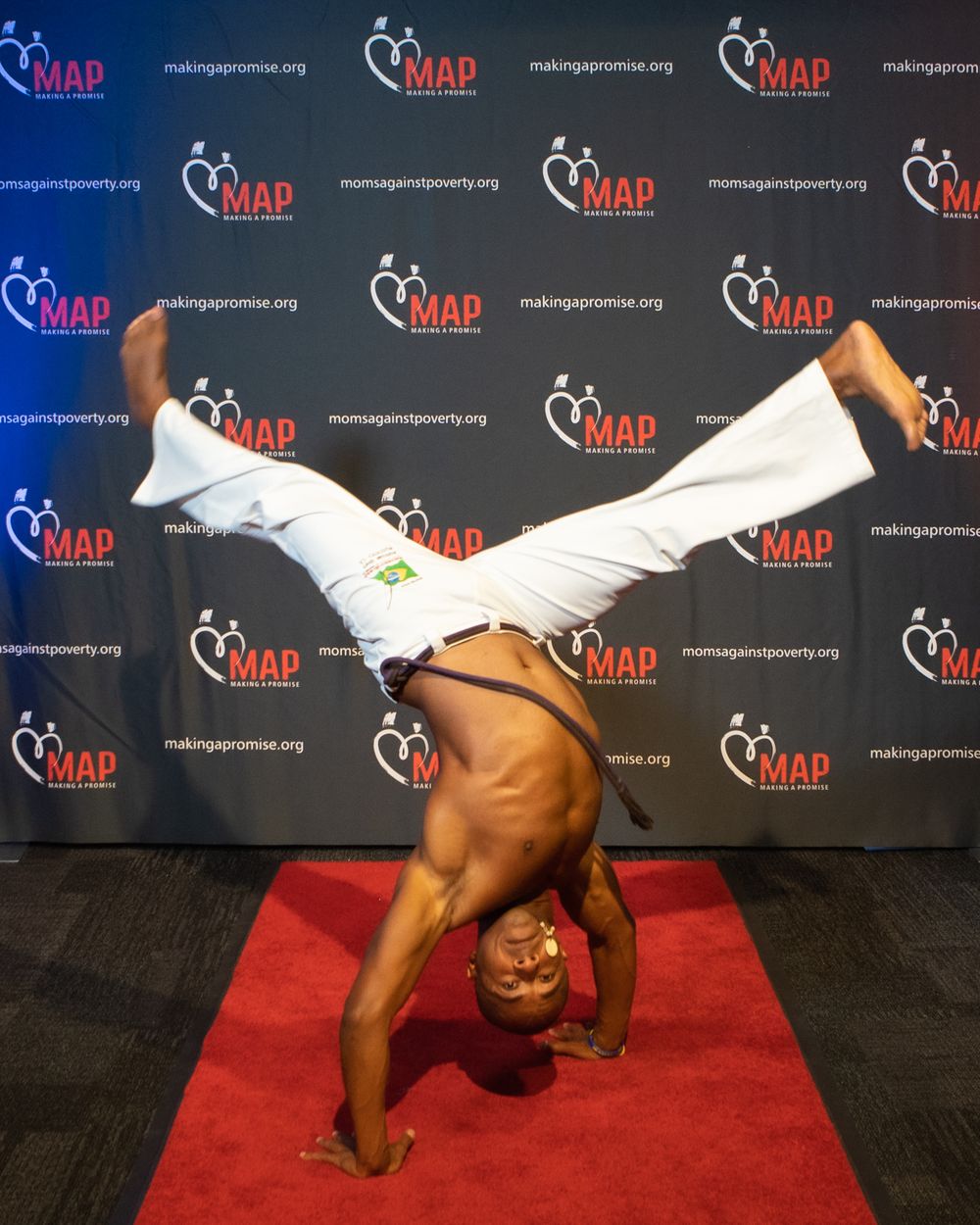Someone performs an impressive handstand on a red carpet in front of a branded step-and-repeat backdrop.