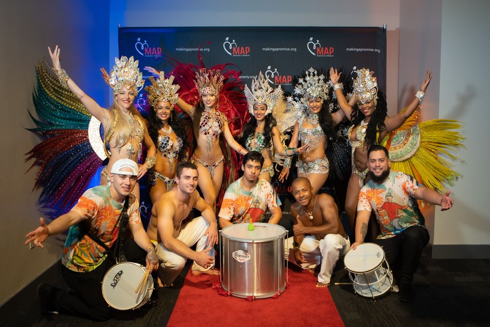 Energetic performers in colorful costumes and feathers pose together in formation for a theatrical show.