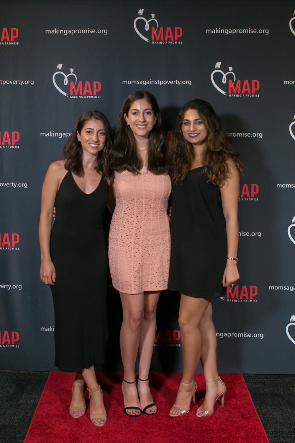 Three women pose together at an event with MAP branding backdrop and red carpet.