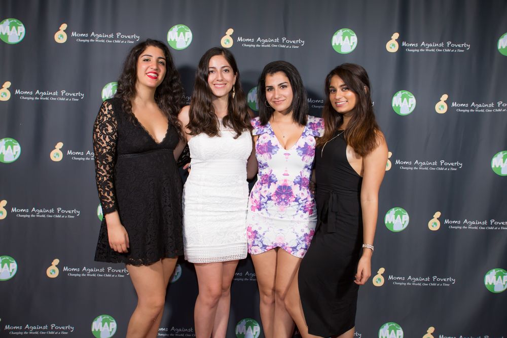 Four friends pose together at an event backdrop wearing black and floral party dresses.