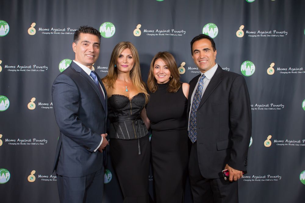 Four people in formal attire pose together at an event with a dark green branded backdrop.
