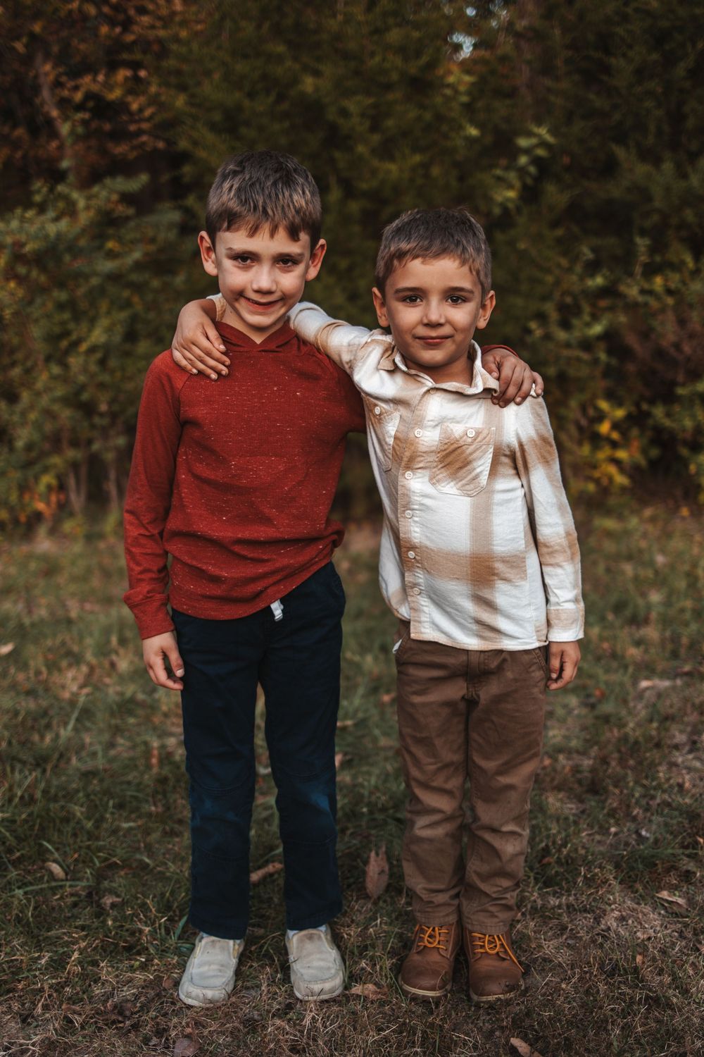 Two young friends in autumn attire stand together in warm lighting outdoors during golden hour.