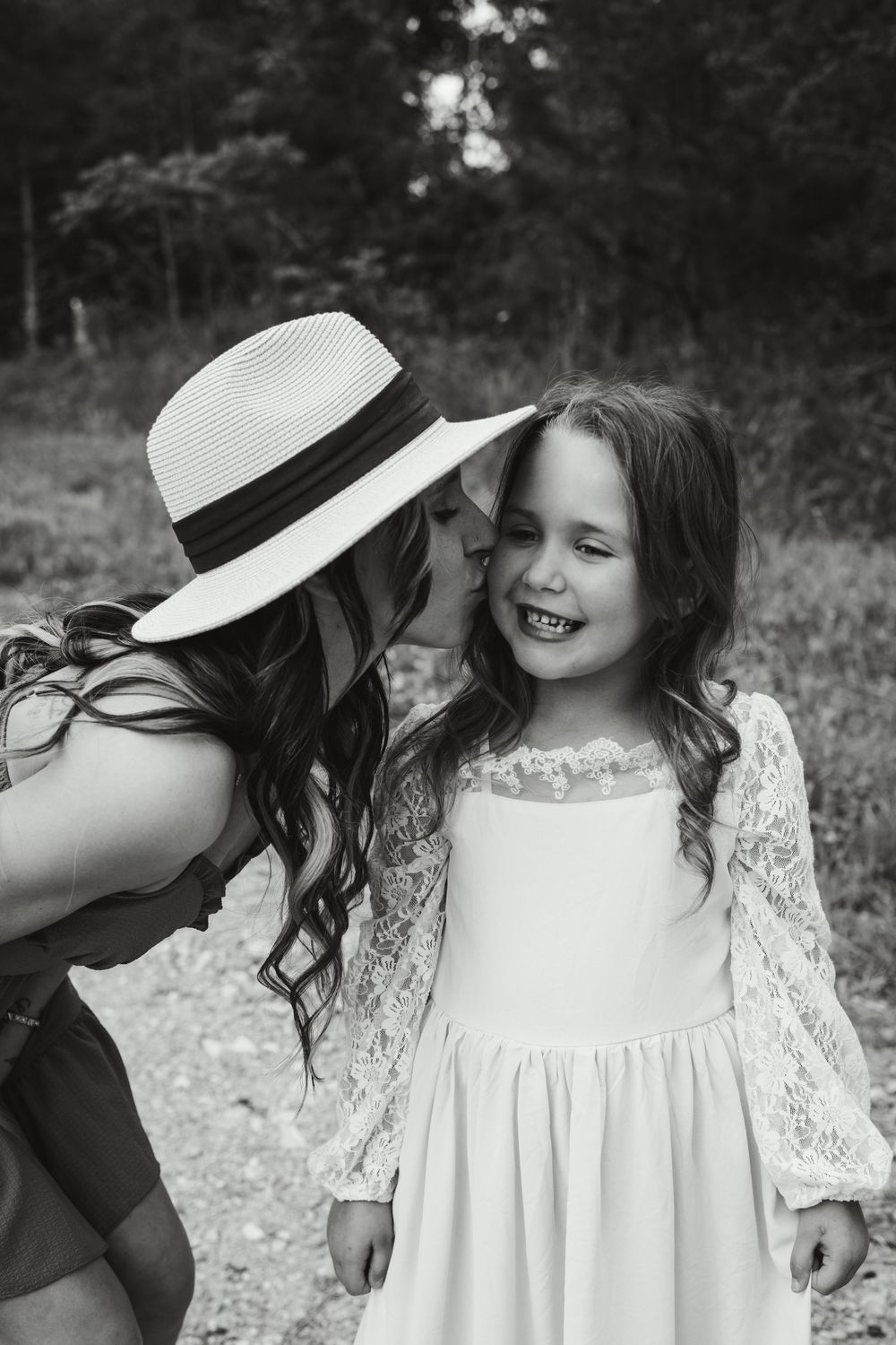 Sweet monochrome photo of a girl in white lace dress sharing an intimate moment with someone wearing a sun hat.