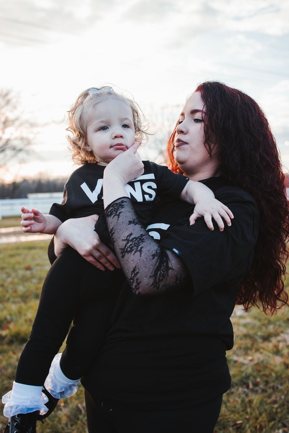 Mother and child in matching black VANS outfits embrace during golden hour sunset in a grassy field.
