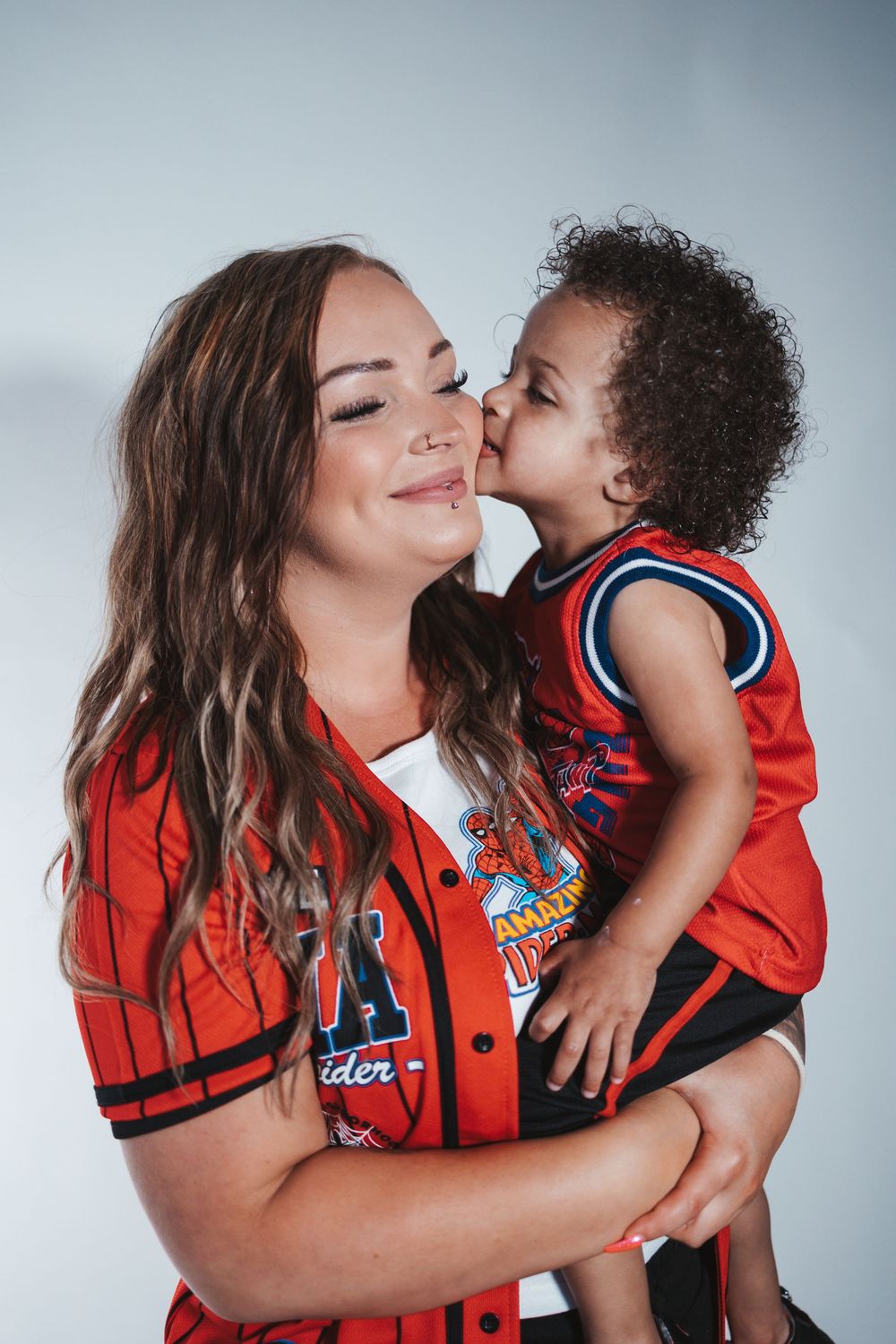 A touching series of photos showing tender moments between parent and child wearing matching red sports jerseys against a gray backdrop.