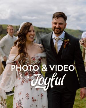 A happy couple shares joyful moments while walking outdoors in wedding attire on a sunny day.