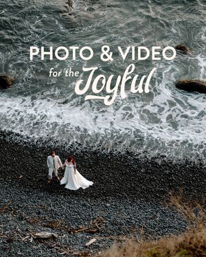 Two people in wedding attire stand against a dramatic black sand beach with crashing ocean waves in Iceland.