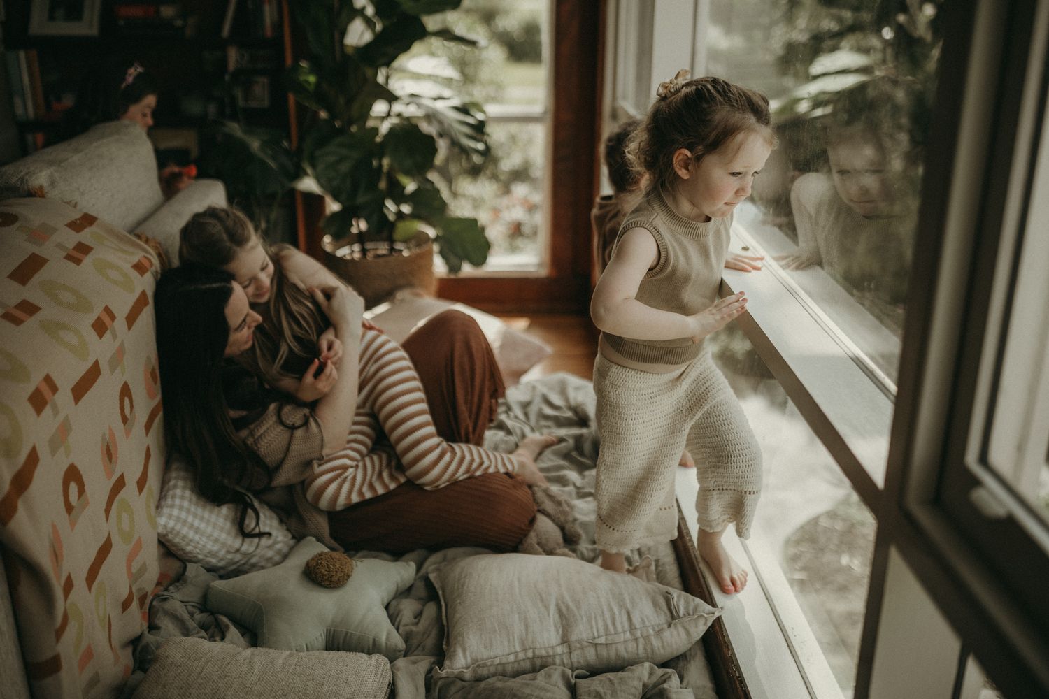 Family sharing a cozy moment together by large windows with indoor plants and natural light streaming in.