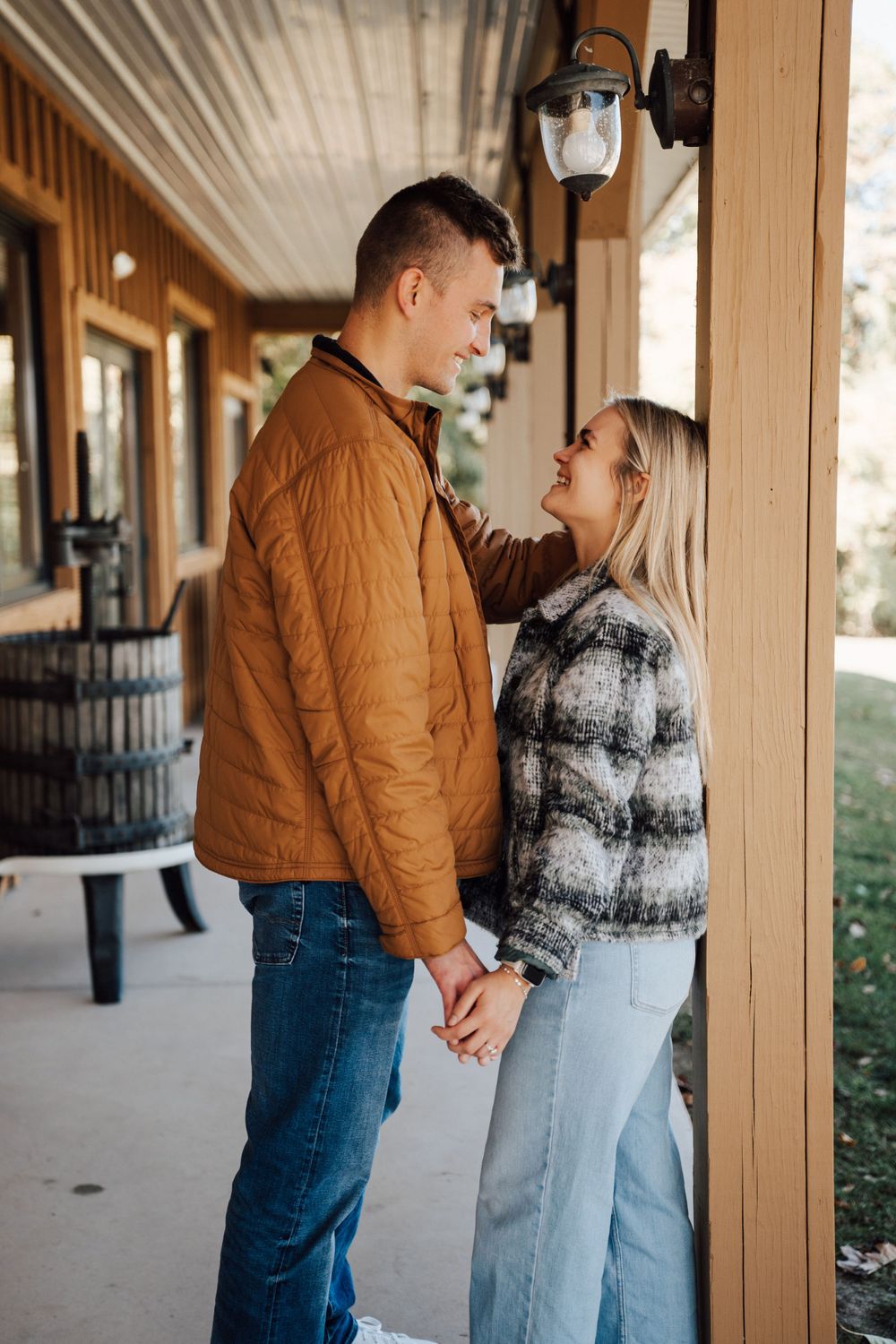 A romantic couple sharing an intimate moment on a covered porch wearing fall attire.