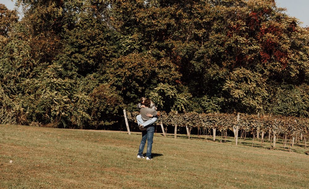 Person spinning joyfully in fall field with vineyard backdrop.