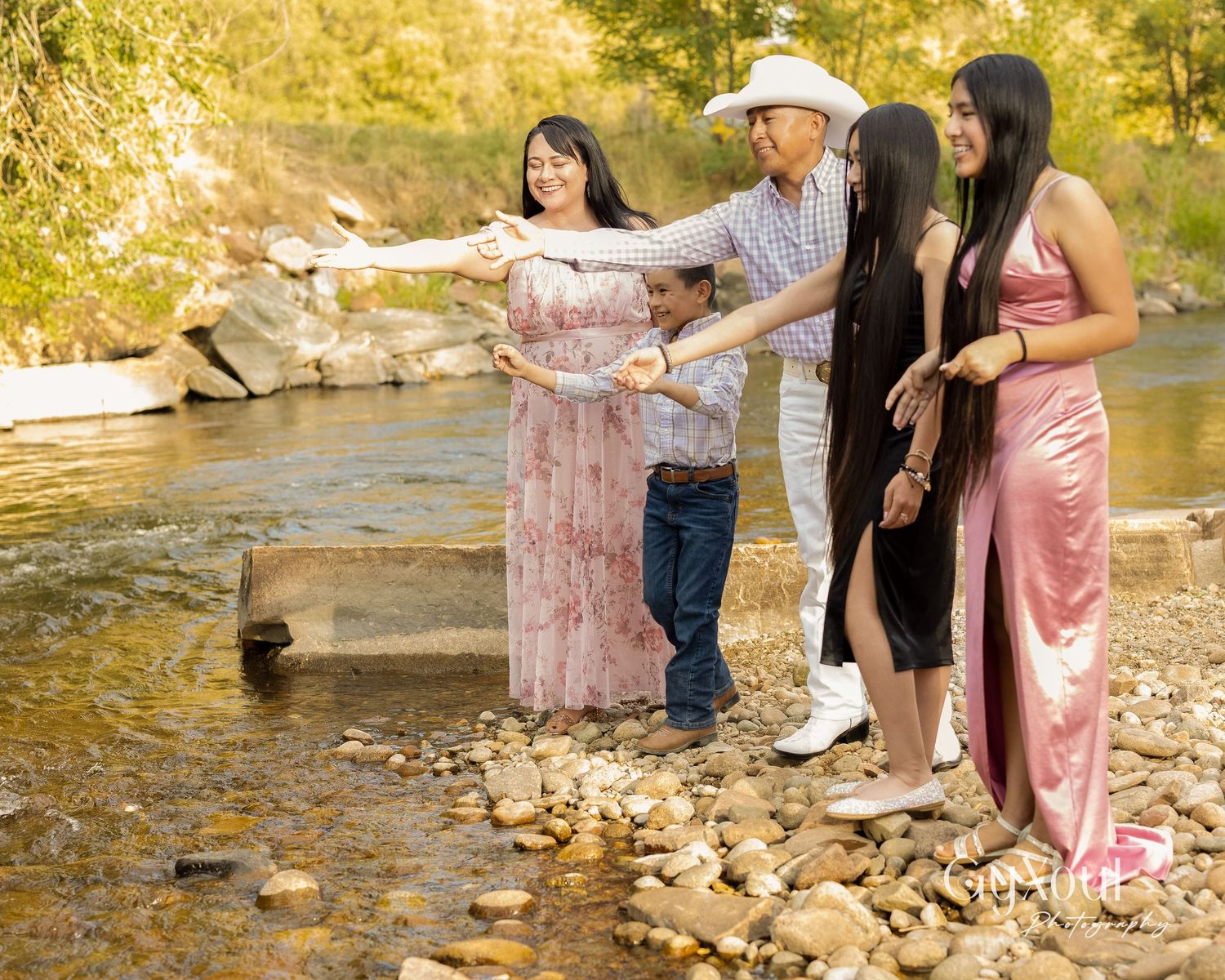 Group stands together on rocky riverbank pointing at something in the distance.