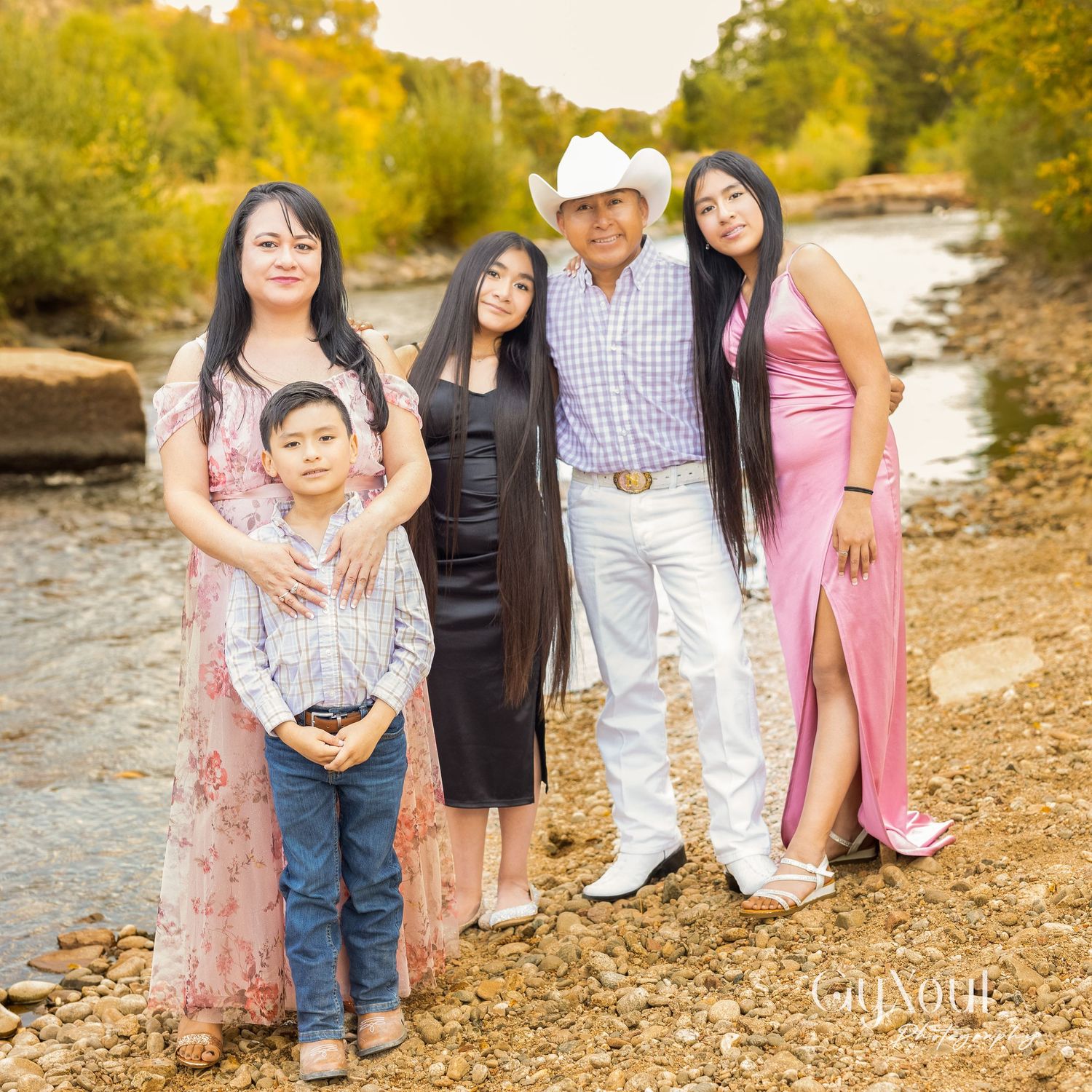 Group portrait taken by riverside wearing coordinated formal outfits in pink, black and white.