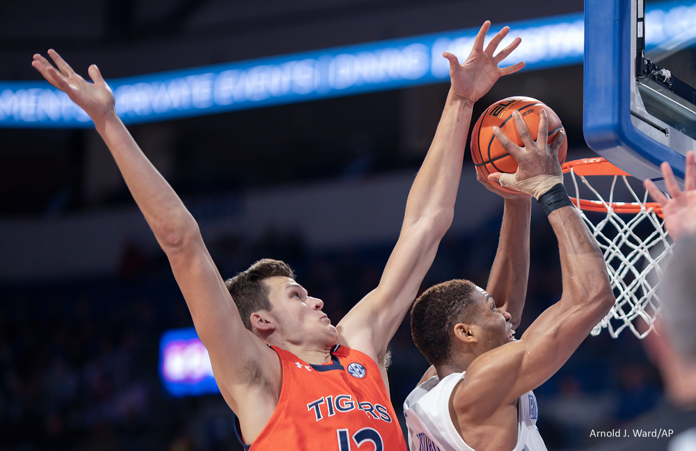 Basketball players jump high competing for a rebound near the basket during an intense game moment.