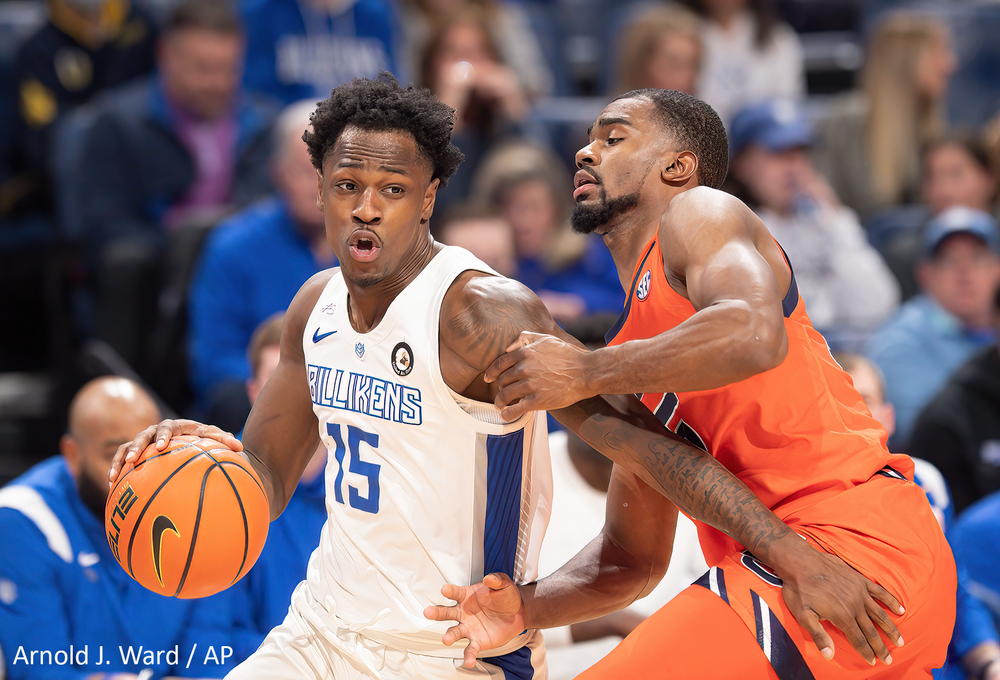 Two basketball players in orange and white uniforms battle for possession during competitive play.
