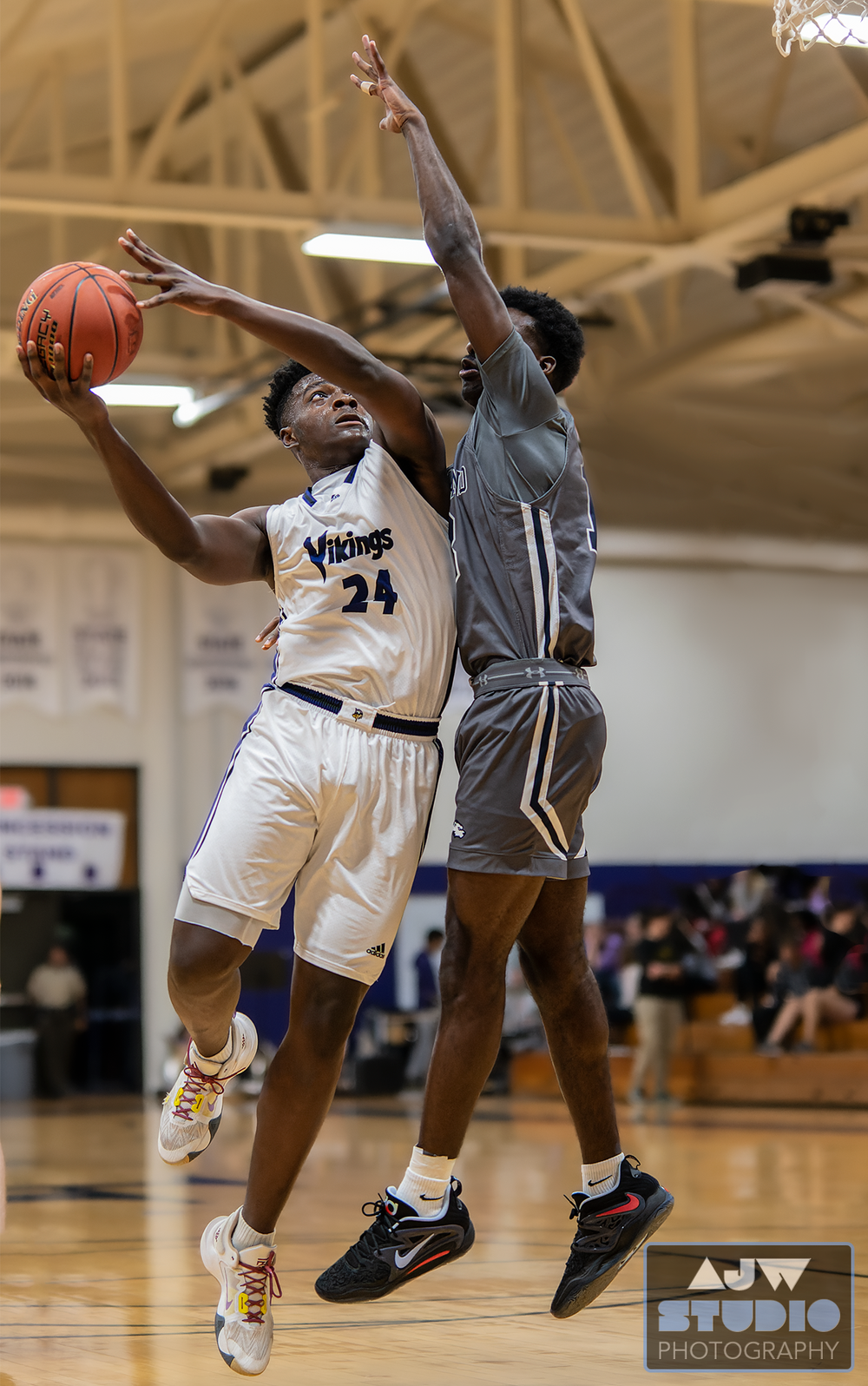 Two basketball players leap high in a game, with one attempting a shot while the other defends.