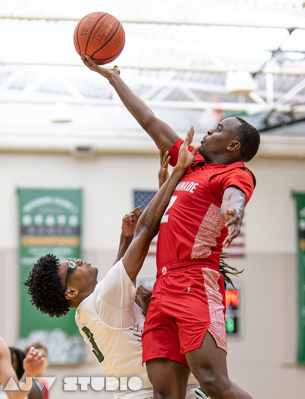 Basketball players leap for contested shot during indoor game.