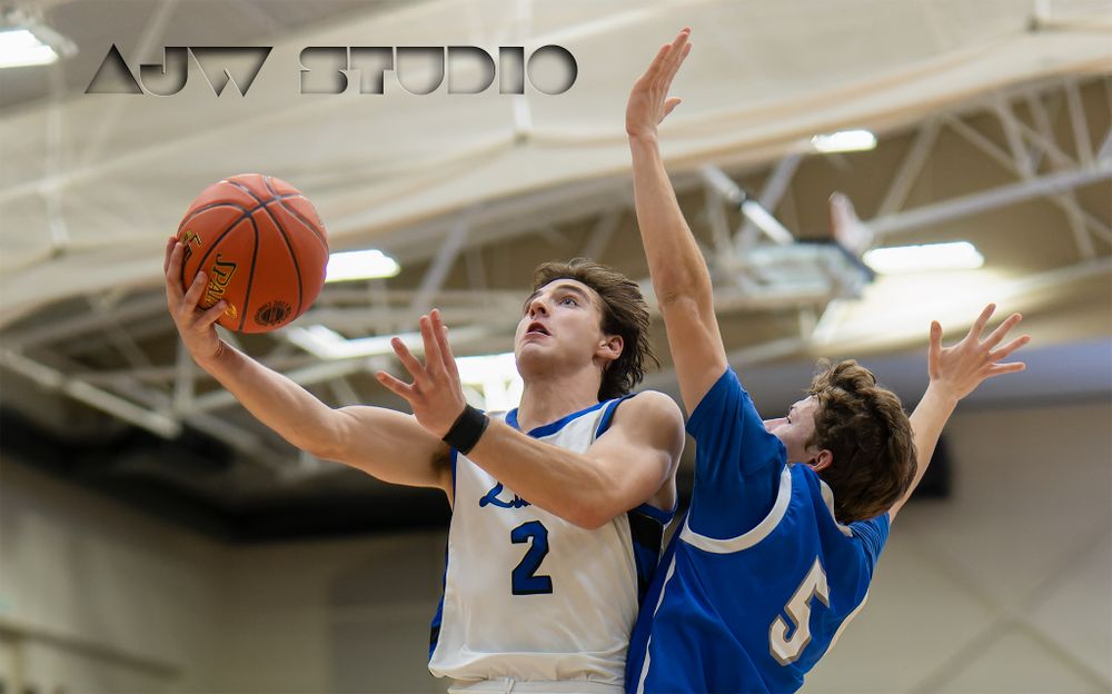 Basketball player drives to basket against defender during indoor game.