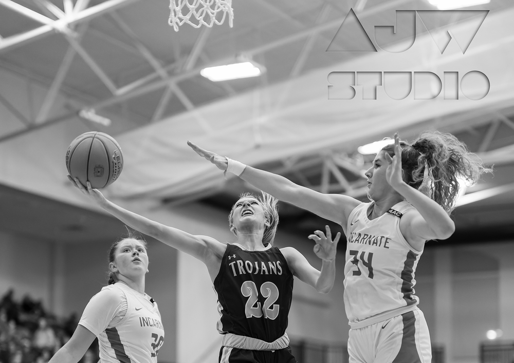 Basketball players compete for rebound in black and white action shot.