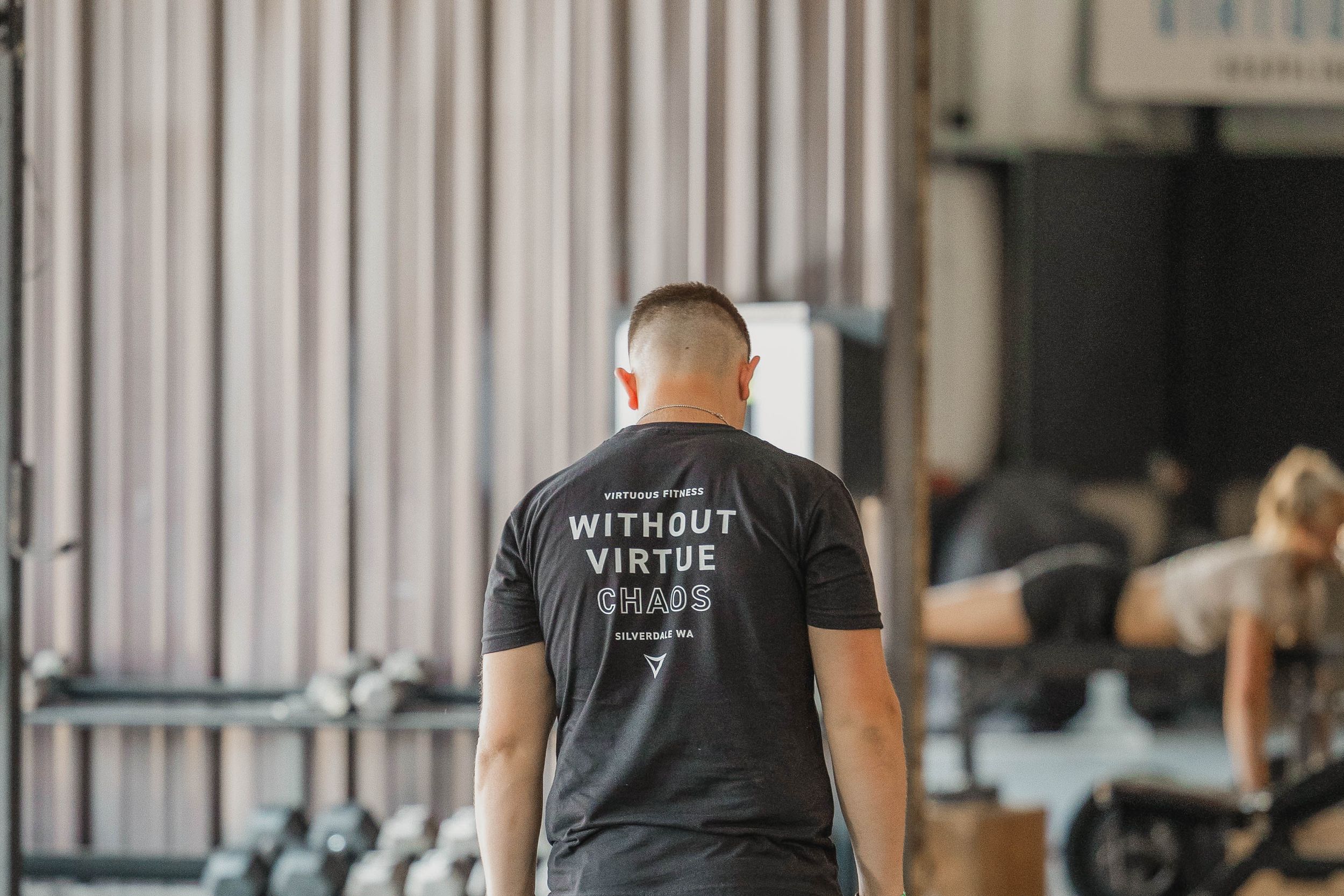 Person wearing a black t-shirt with text shows back view in fitness facility setting.
