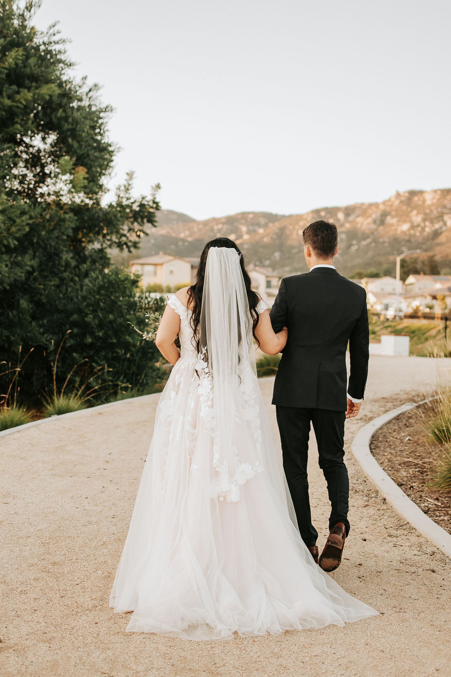 Newlywed couple walking down a winding path with mountain views in the background.