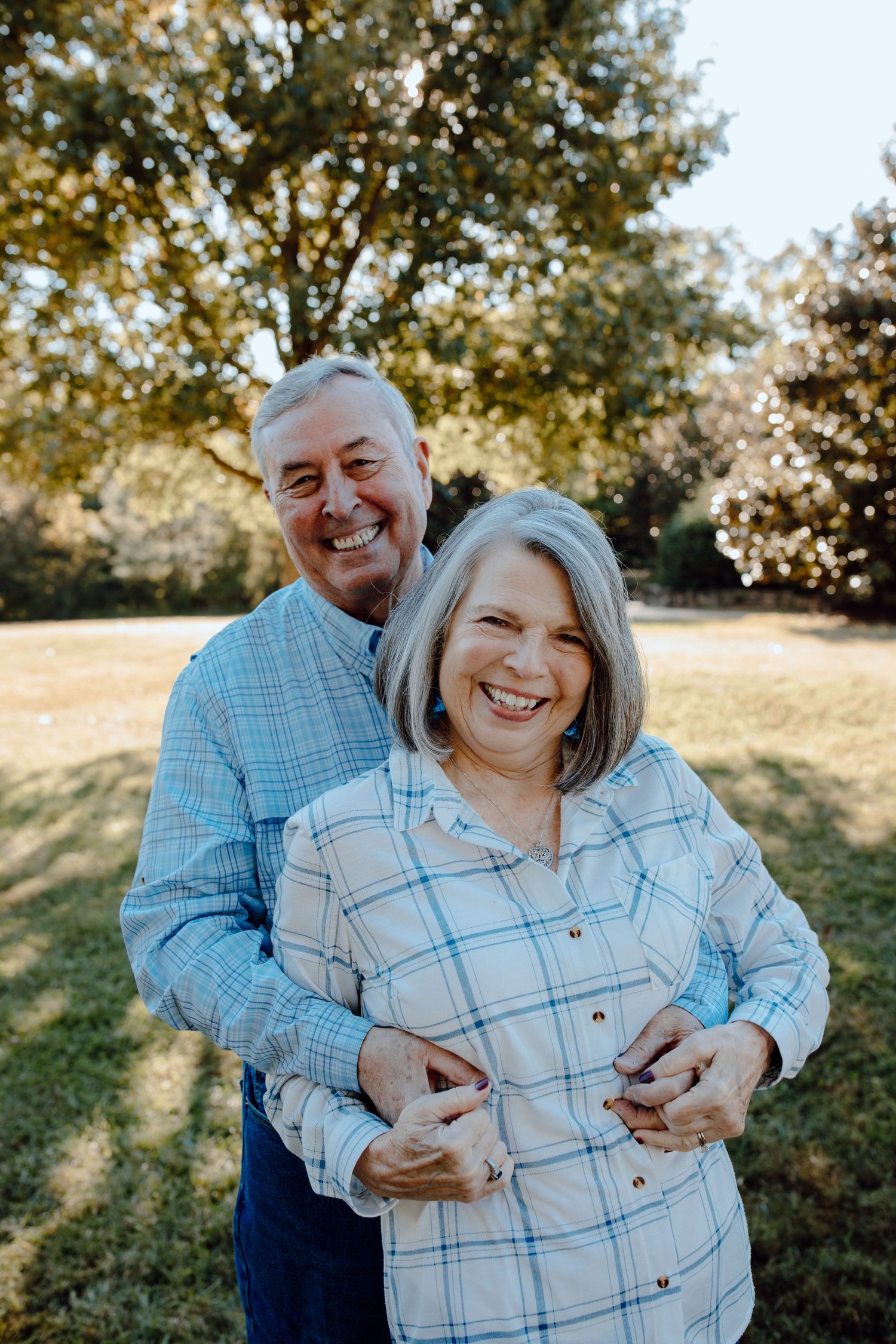 A mature couple embraces while laughing together outdoors on a sunny autumn day.