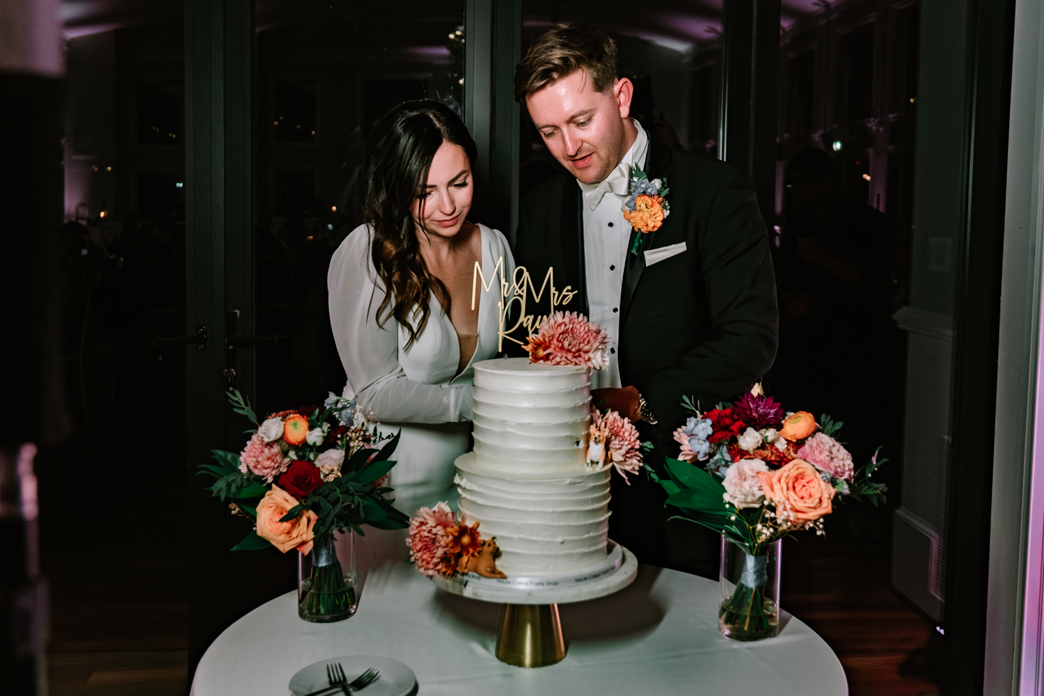 A couple cuts their white wedding cake decorated with fresh coral and peach flowers.