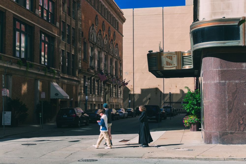 People walking in an urban street with historic architecture and shadows.