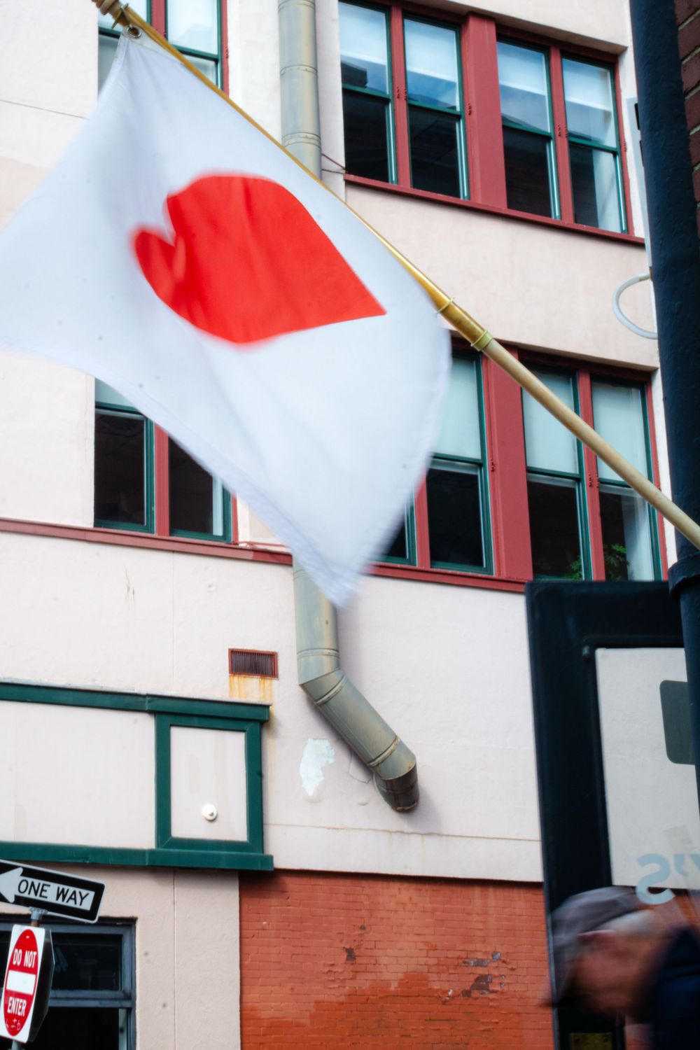 Japanese flag with red circle hanging from a modern building with red-trimmed windows.